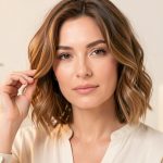 Portrait lumineux d’une femme adulte aux cheveux courts ondulés, avec des produits capillaires vegan minimalistes flous en arrière-plan.