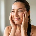 Une jeune femme se rafraîchit le visage à l’eau après une séance de sport, dans une lumière douce et naturelle.